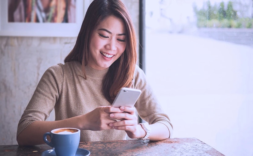 Woman sitting at cafe smiles at smart phone in her hand