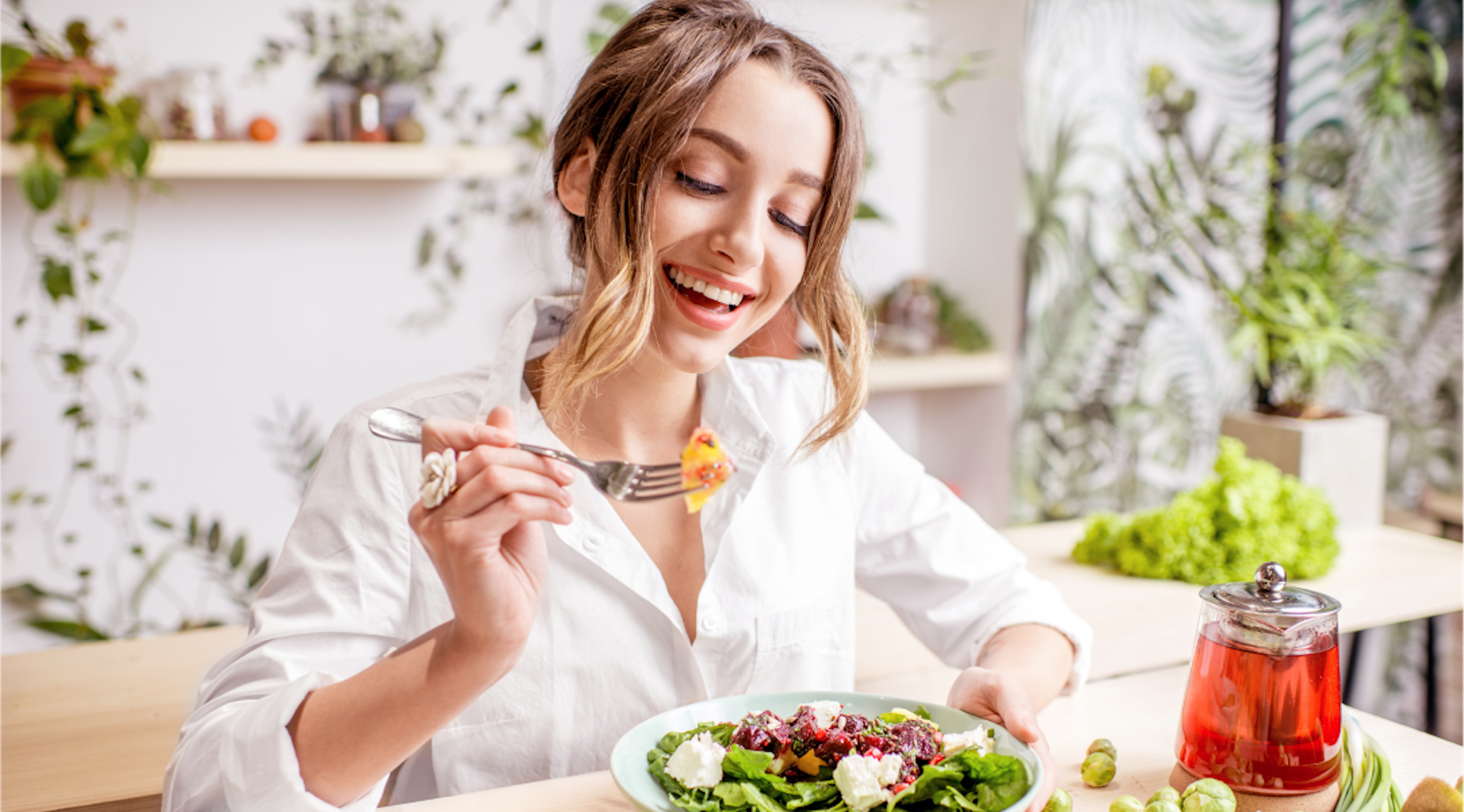 woman smiling at her salad she's eating at a dining table.