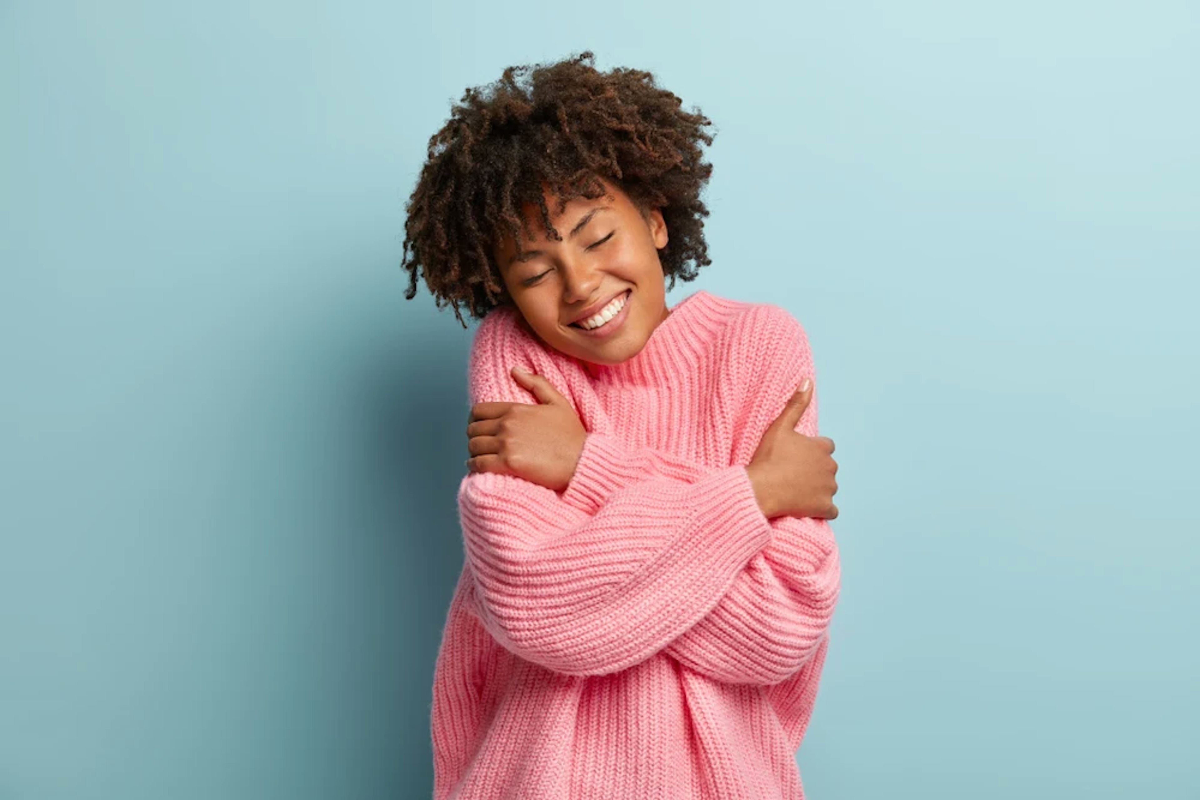 Woman giving herself a big hug in a comfy pink sweater