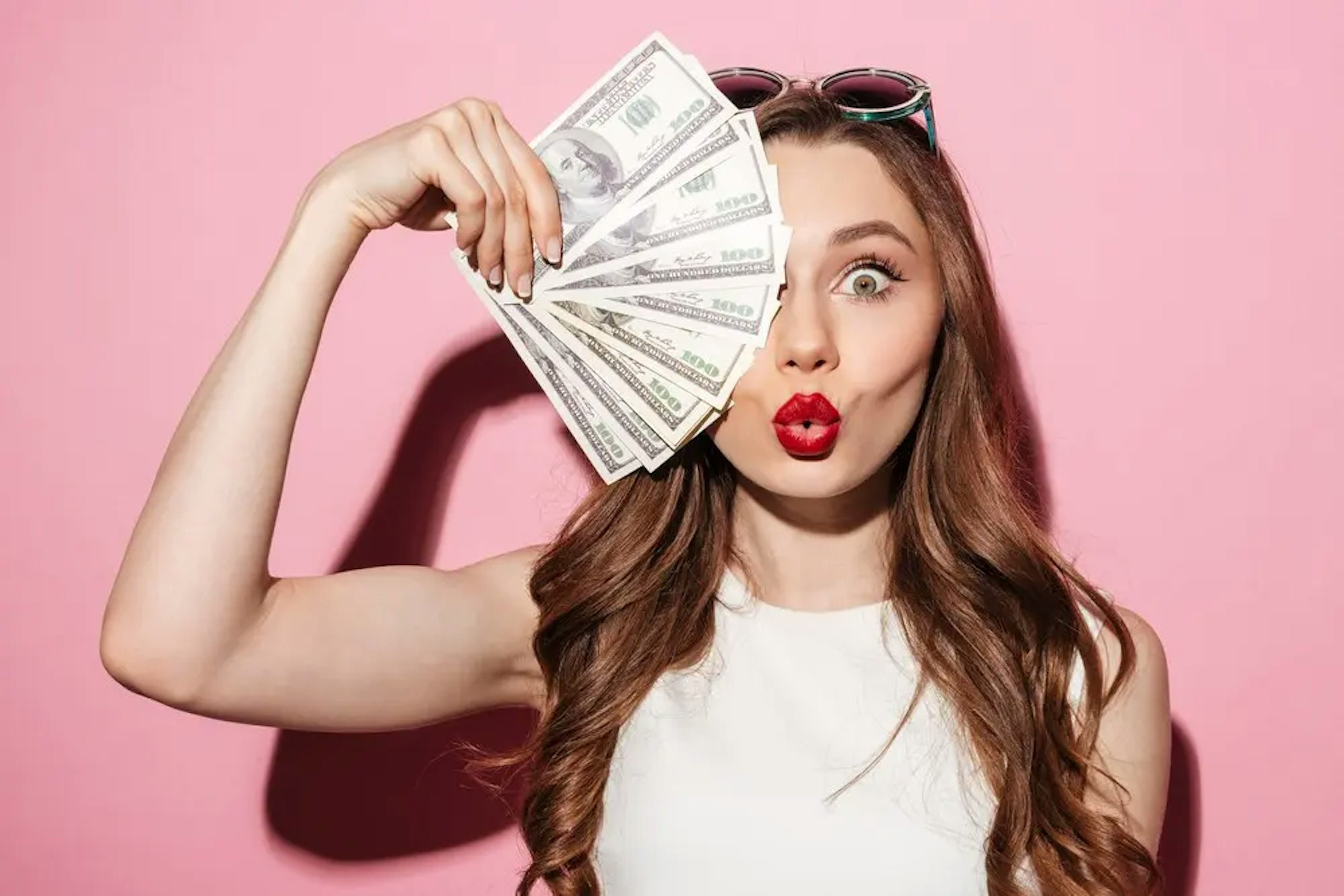 A woman wearing red lipstick holds a stack of cash fanned out over one eye