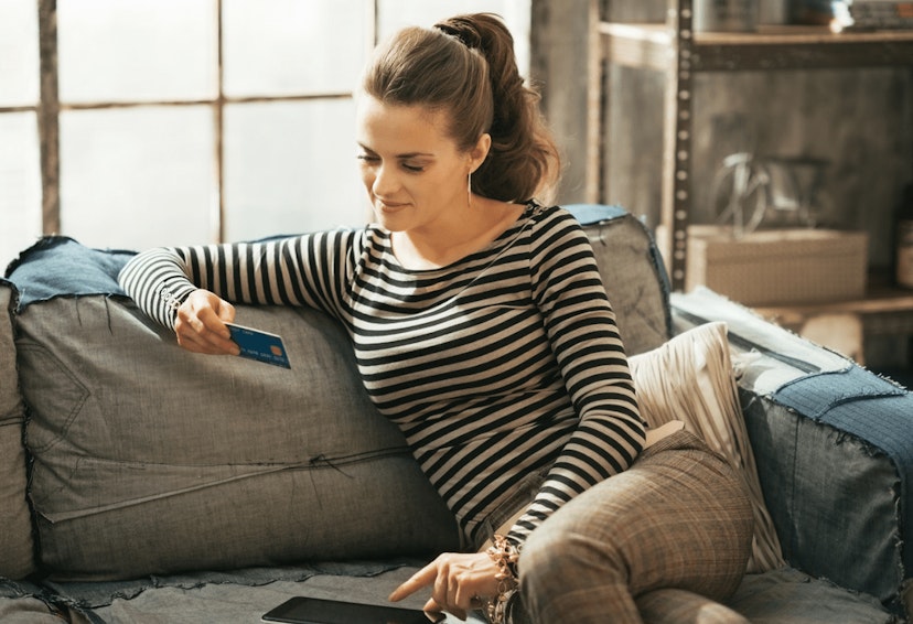 Woman on phone looks at a credit card in hand.