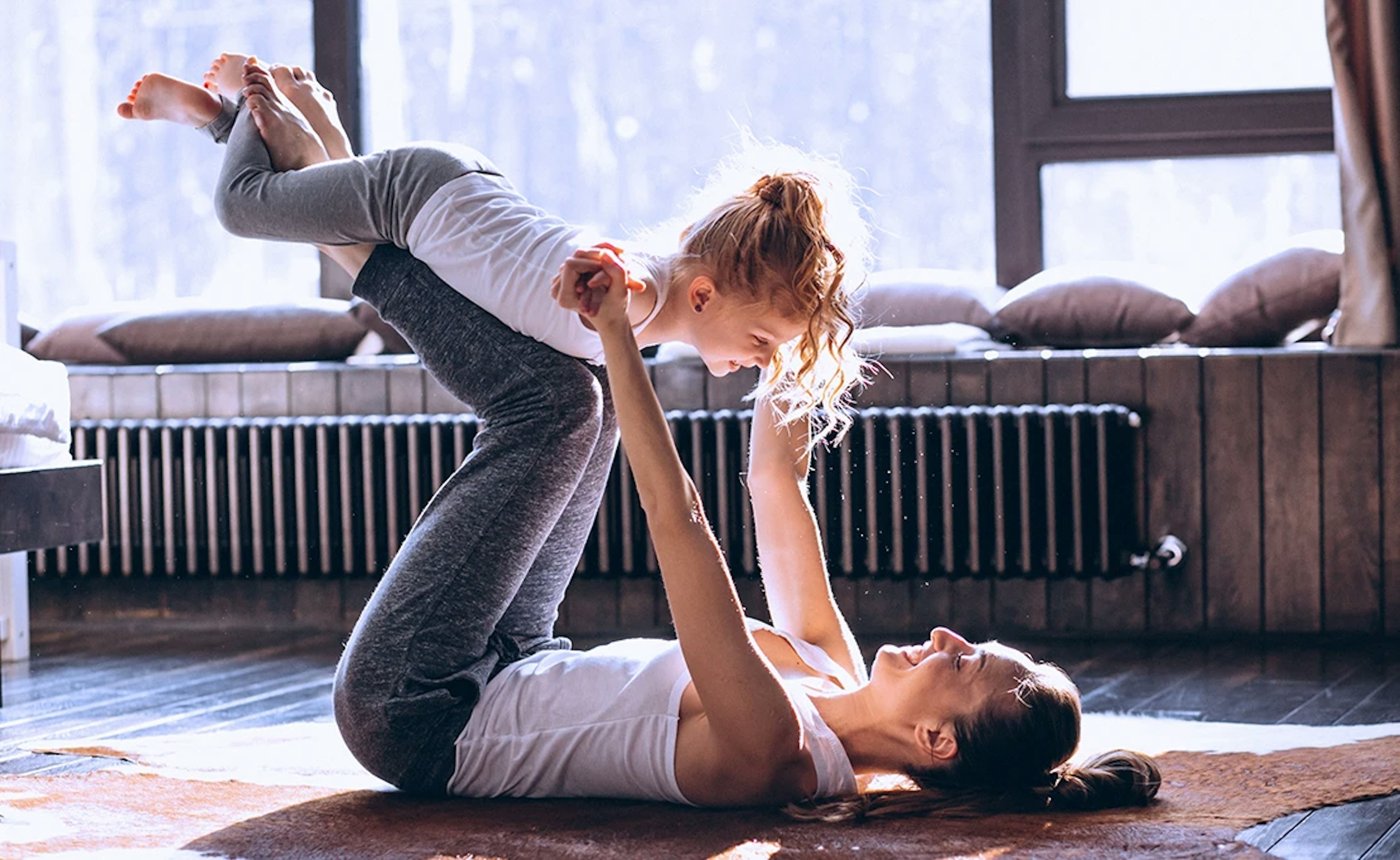 A woman on her back holds up a child with her feet and legs