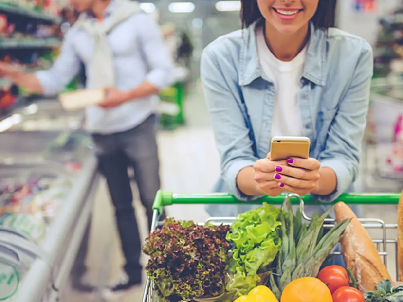 A woman at the grocery store looks at her phone for Ibotta cash back