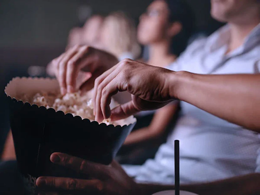 People in a movie theatre with hands in popcorn bags, saved money with Ibotta