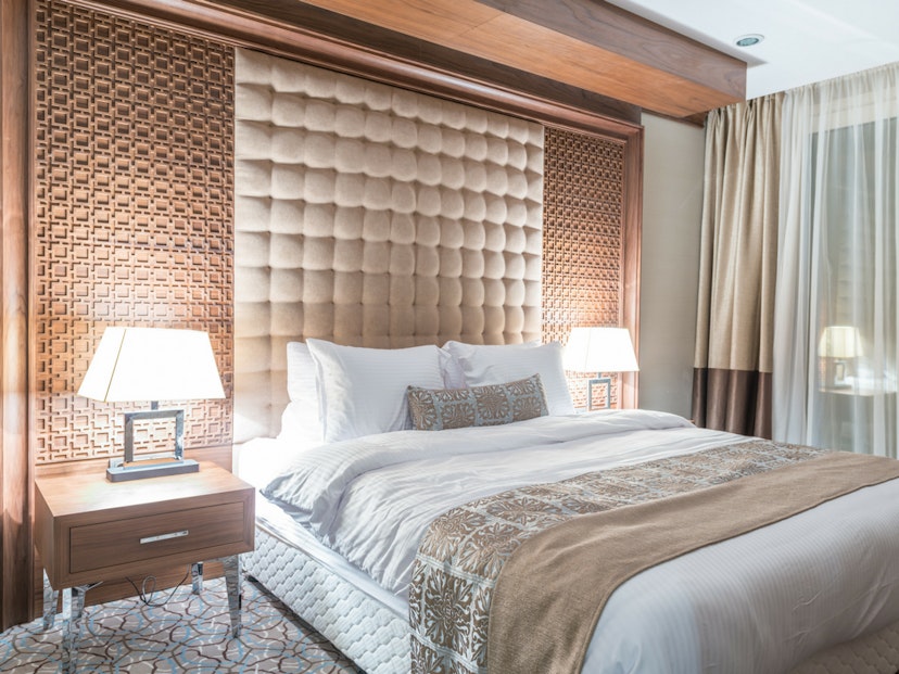 a warmlit hotel room with white bedding and cream sheets and tufted headboard.