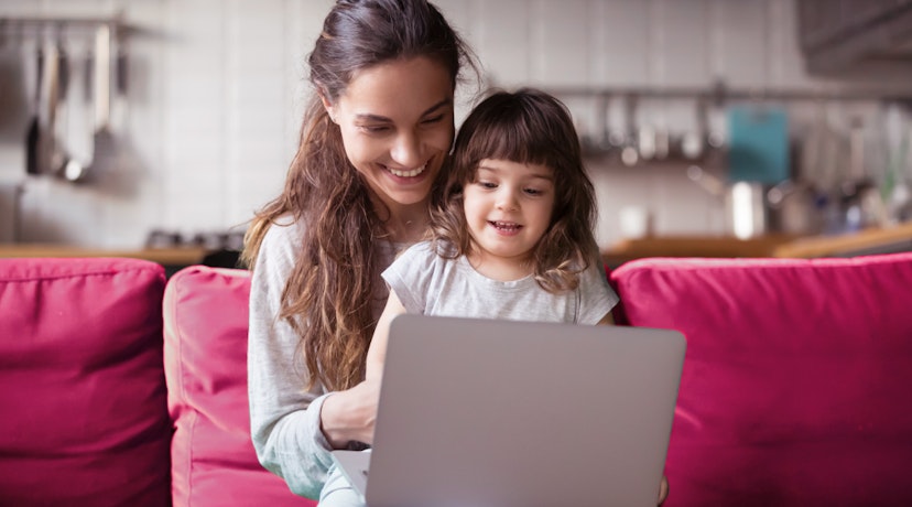 Woman on couch sits with child in lap. They're looking at a laptop on a coffee table before them.